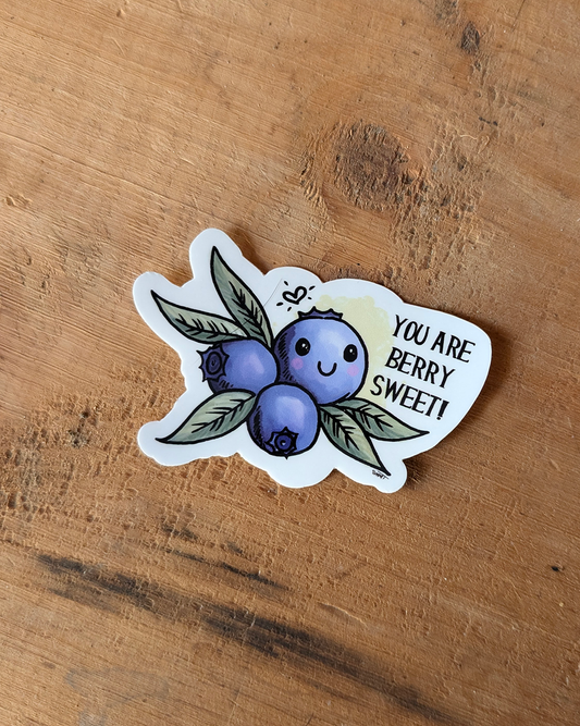 A vinyl sticker with a illustration of a smiling blueberry with leaves and the phrase 'YOU ARE BERRY SWEET' written alongside.