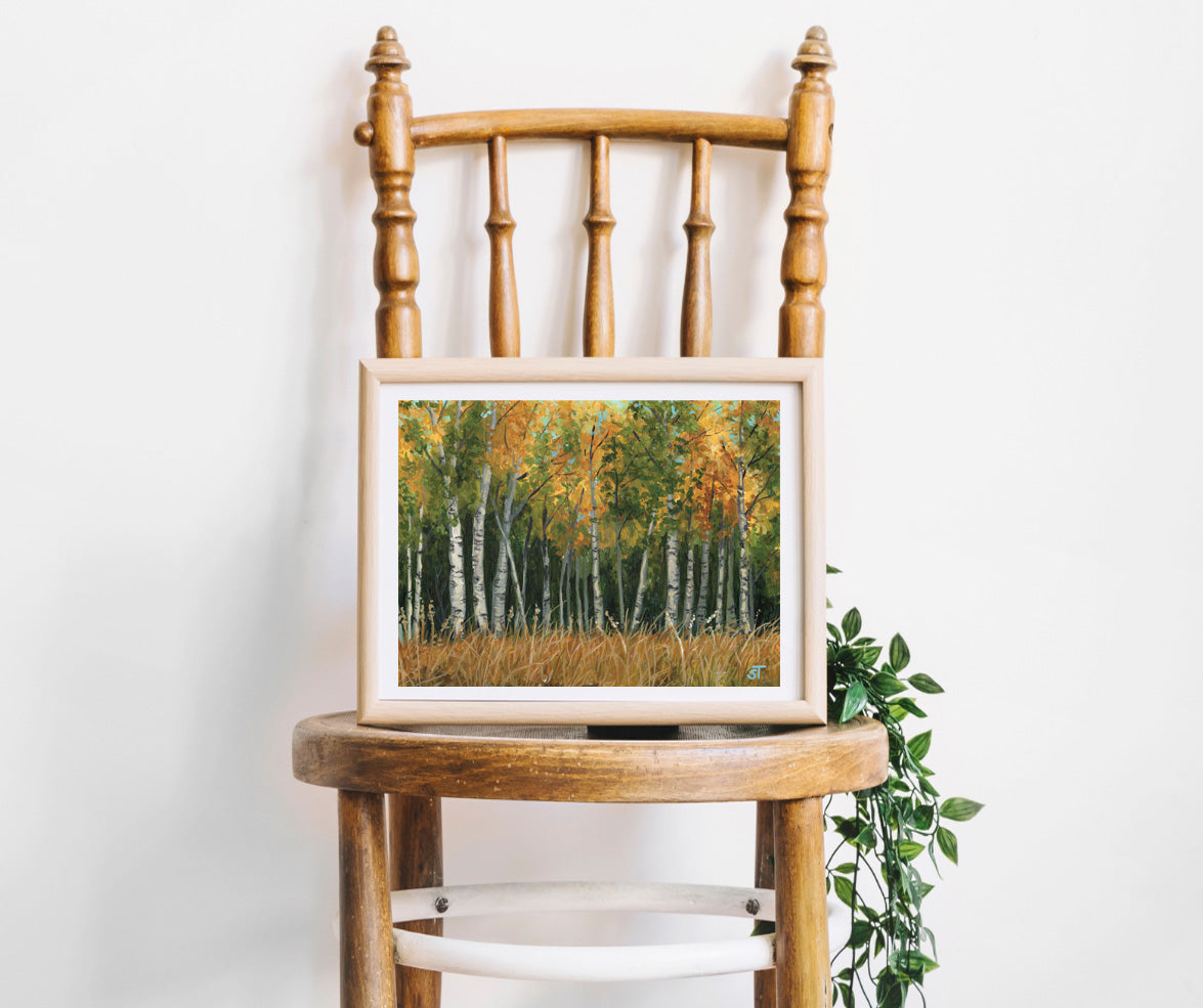 Framed artwork of a forest scene on a wooden chair against a white wall.