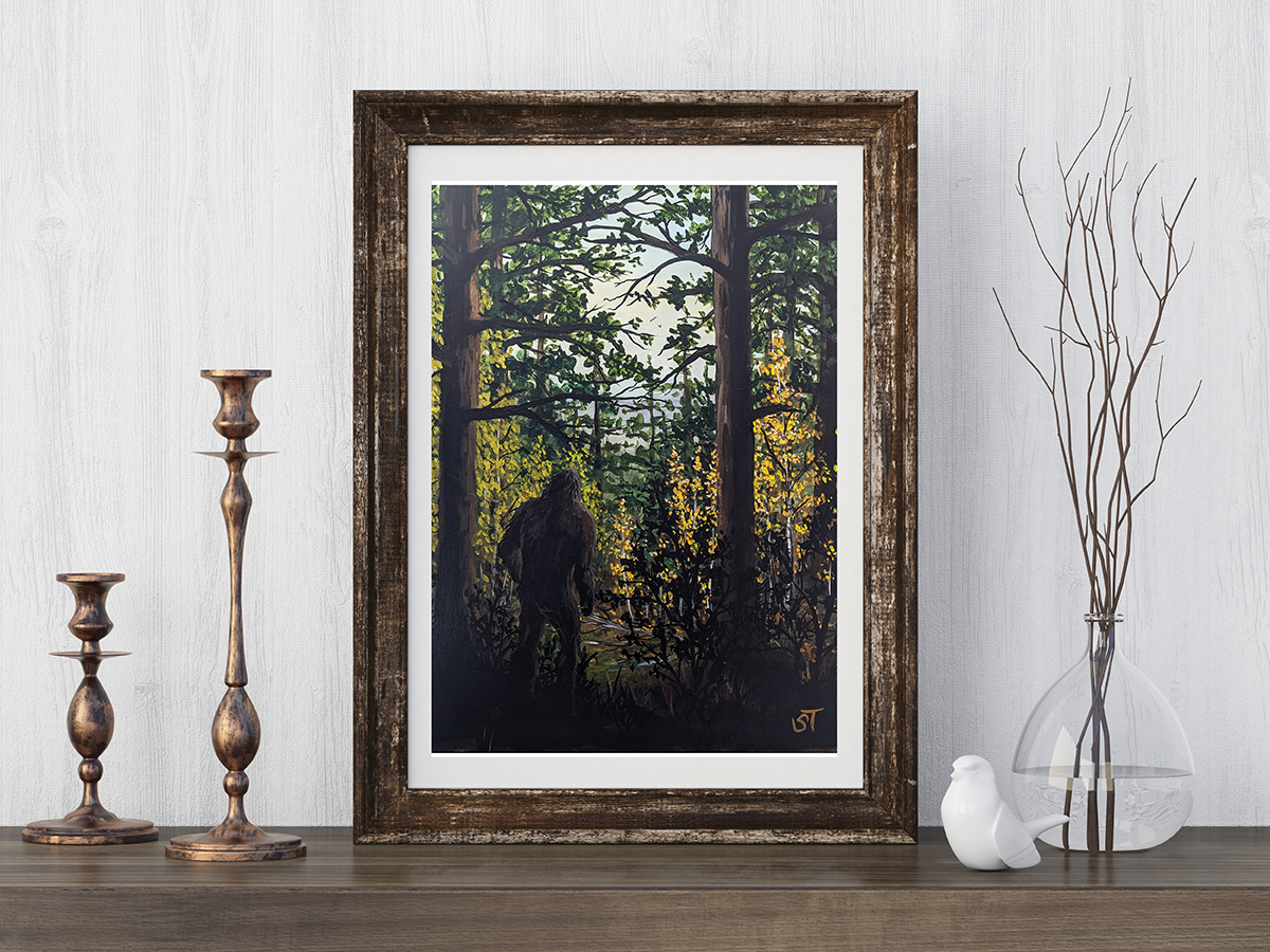 Framed cryptid art print of a shadowed Sasquatch walking through a dense forest, golden light filtering through trees as the elusive figure moves between trunks, styled on a wooden shelf with rustic decor.