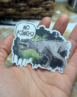 Sticker of a tyrannosaurus with 'No Kings!' text held in a hand.