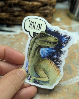 Sticker of a dinosaur with 'YOLO!' speech bubble held by a hand