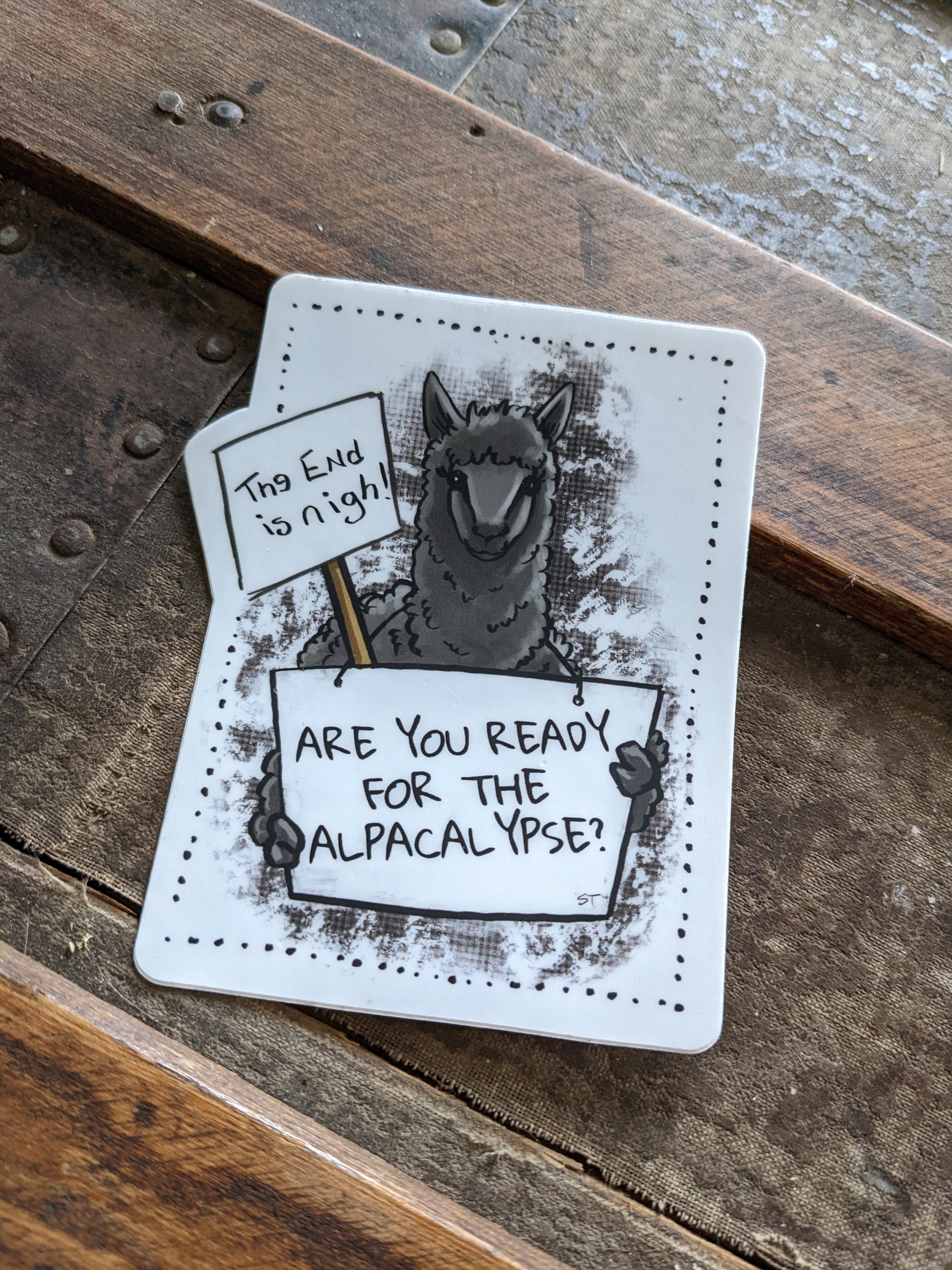 Vinyl sticker featuring a dark illustrated alpaca holding a sign that reads “Are you ready for the alpacalypse?” with a smaller sign reading “The end is nigh.”