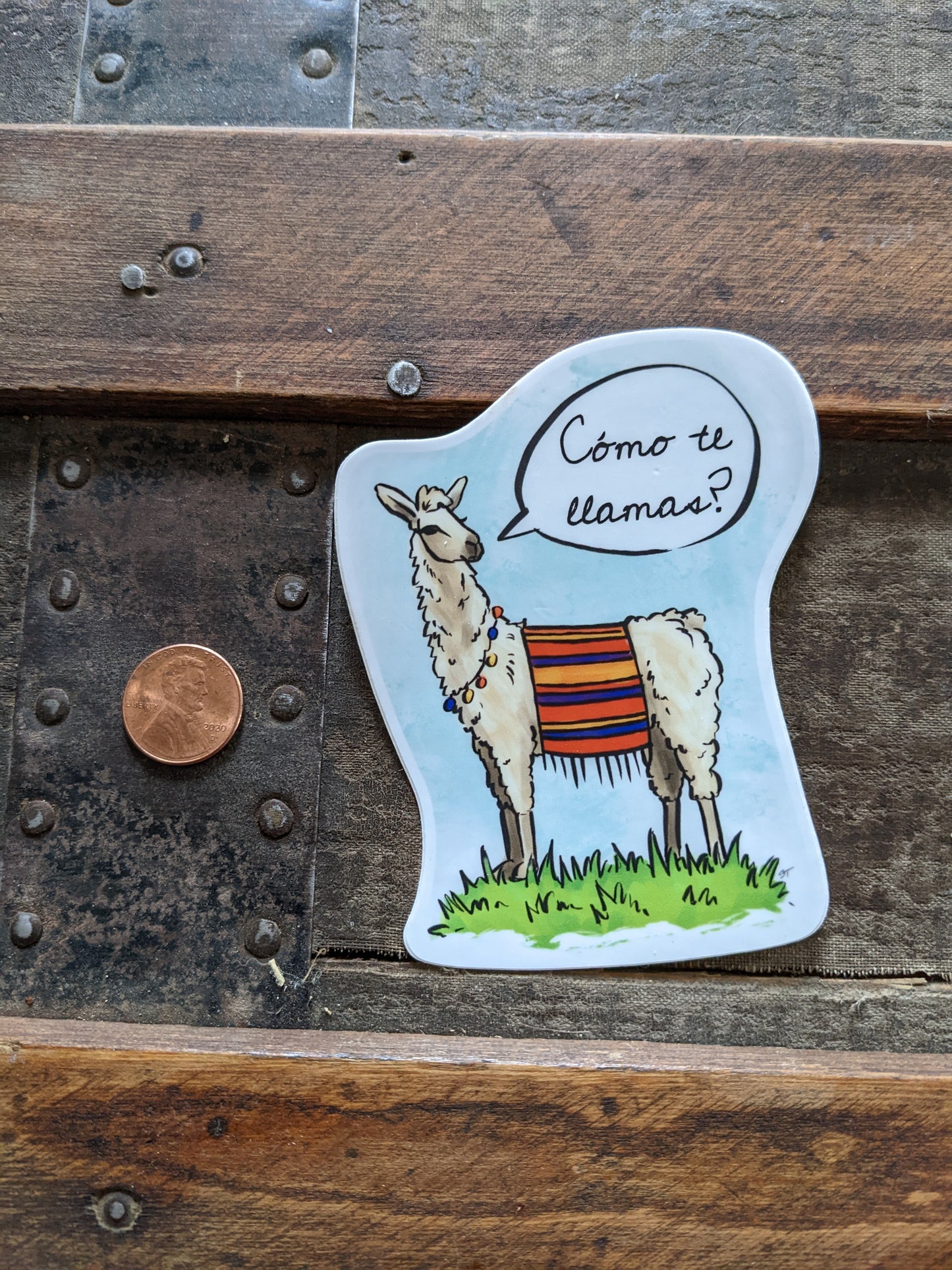 Llama vinyl sticker shown next to a penny for size reference, featuring a speech bubble with the text “¿Cómo te llamas?”