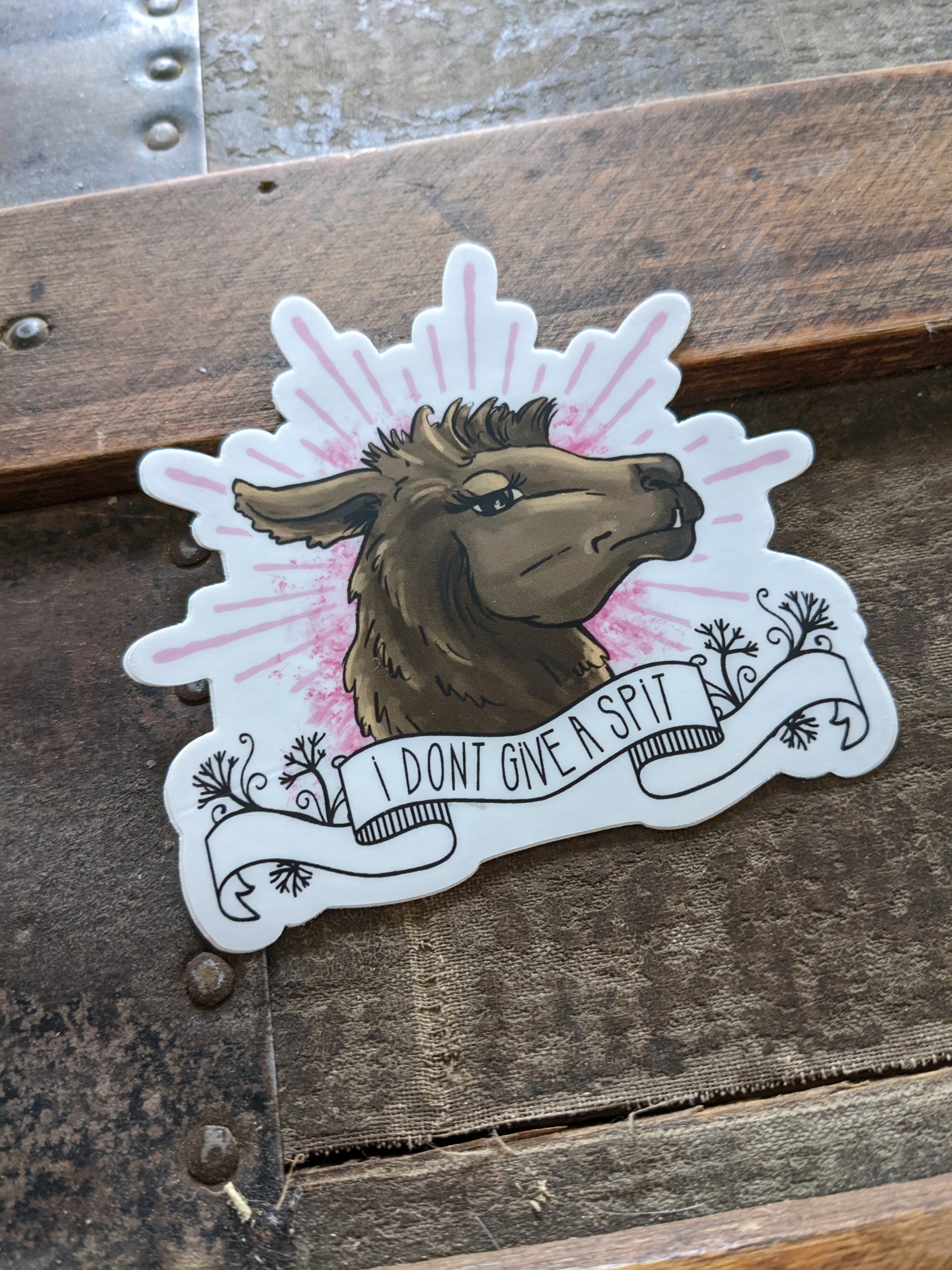 A vinyl decal featuring an illustrated llama with the phrase 'I don't give a spit' written across its body, placed on a wooden surface.
