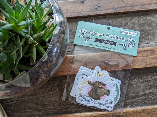 A set of alpaca and llama themed stickers with puns, displayed on a wooden surface next to a glass bowl with a plant.