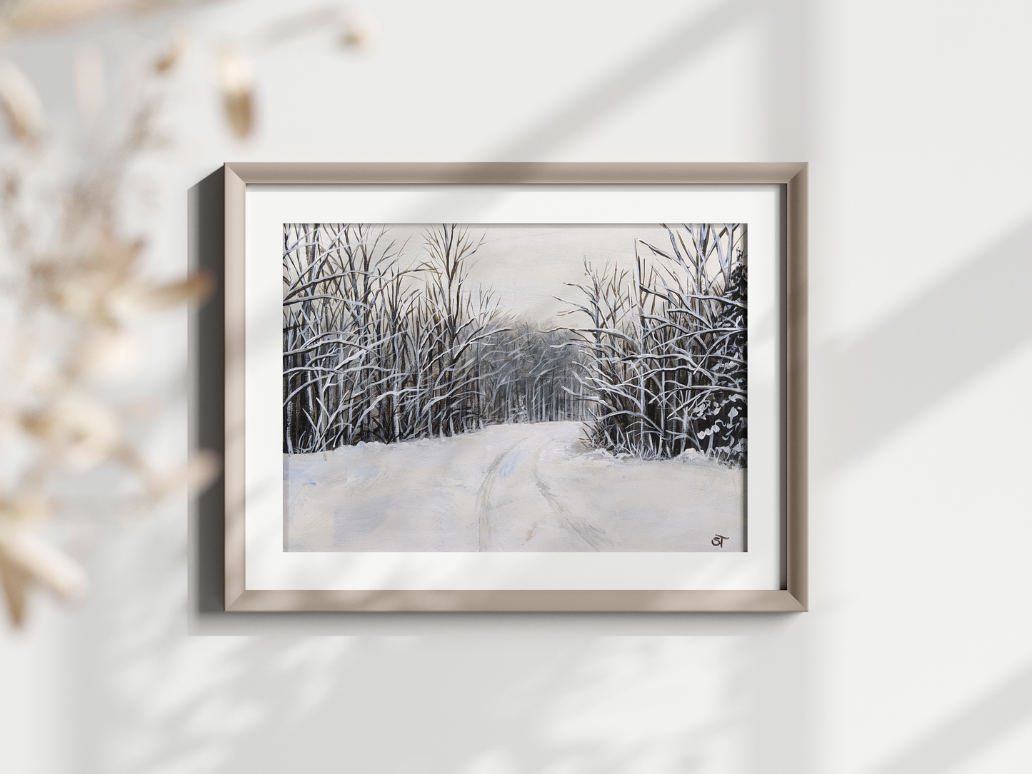 A framed fine art print featuring a winter landscape with snow-covered trees and a rural road, displayed on a white wall.