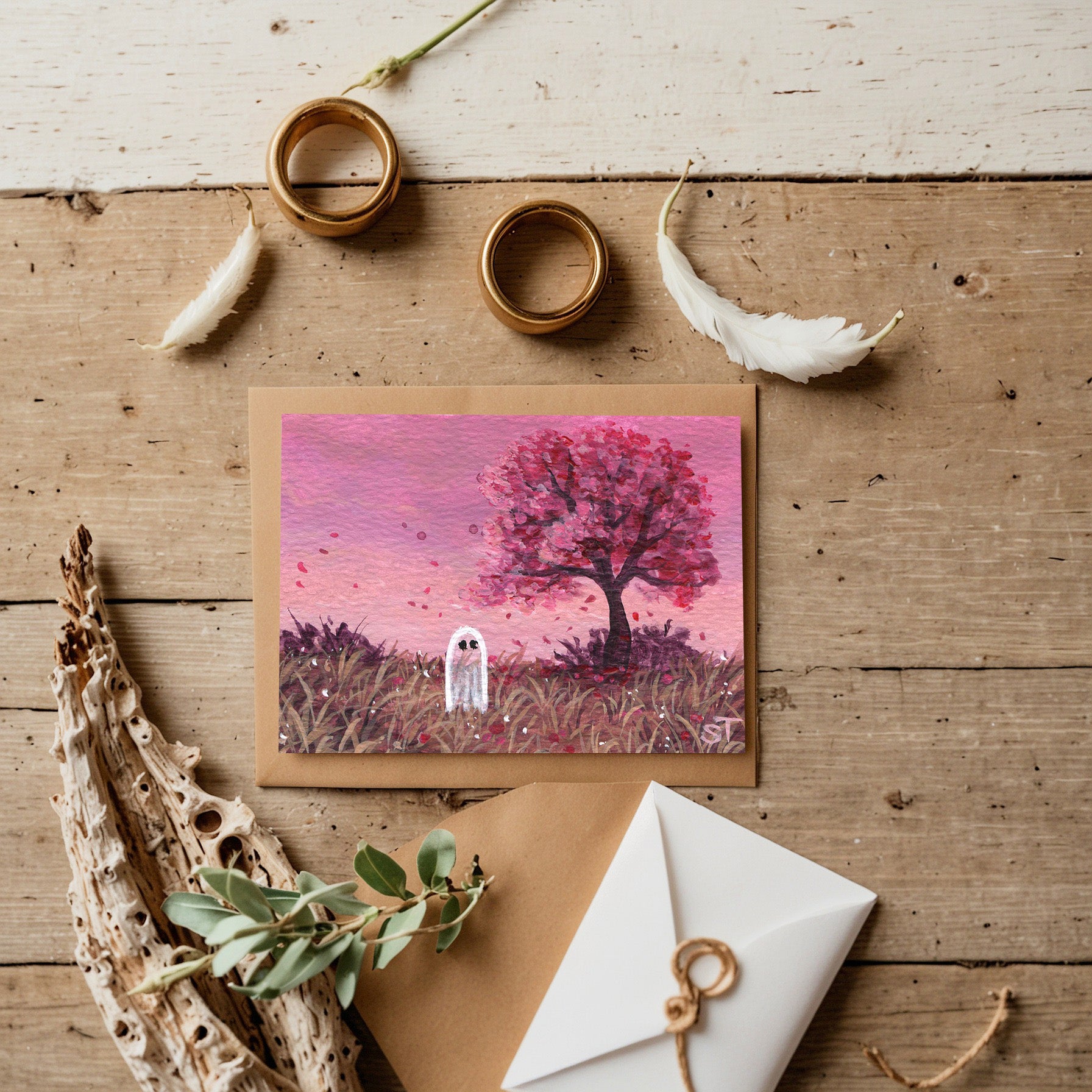 Greeting card with a pink tree and ghost illustration on a wooden surface with decorative items.