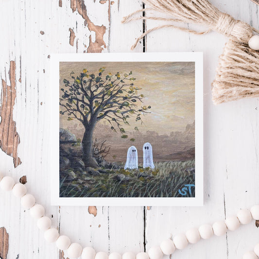Art print of two ghosts under a tree on a rustic wooden surface with decorative elements.