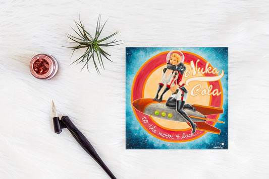 Square greeting card featuring a retro pin-up style female astronaut riding a rocket through space, styled on a white textured surface with a calligraphy pen, ink jar, and small air plant.