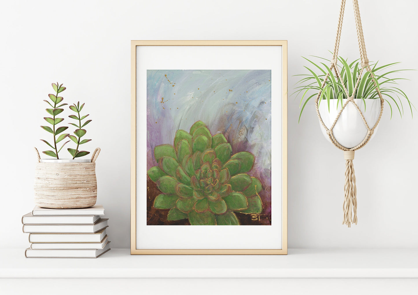 A framed art print depicting a painting of a succulent with an abstract background and gold embellishments, displayed on a wall beside a plant and books.