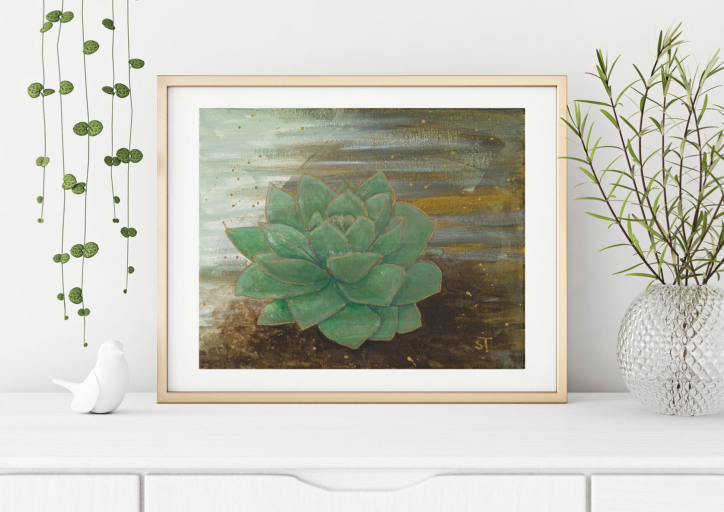 Framed green succulent art print by Sarah Terrell styled on a white shelf with hanging vines and decorative vase.